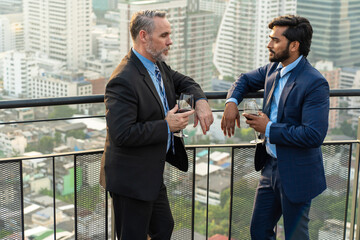 Indian male manager with A male executive in a suit holding a glass of wine cocktail is standing on...