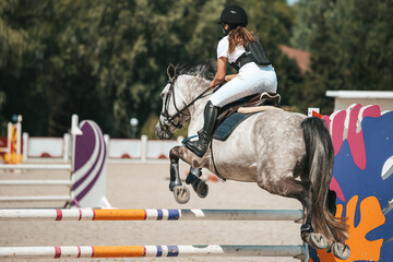 Girl rider in show jumping competition. A rider on a horse jumps over an obstacle. Horseback...