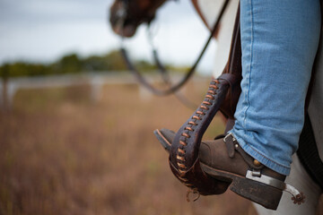Cowboy on horseback at sunset in the field. Focus on the spur. Western boots and stirrups in...