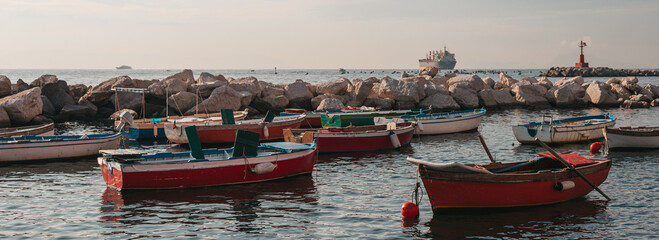 Fototapeta na wymiar Fishing boats in the morning on the Naples waterfront. Traditional boat at the pier, in Italy. Focus on the boat. Cargo ship, fishermen and a lighthouse on the background.