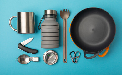 Set of tourist equipment on a blue background. EDC set flat lay. Camping plate, mug, bottle, spoon...