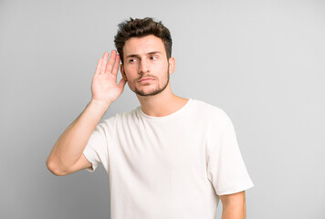 young handsome man looking serious and curious, listening, trying to hear a secret conversation or...