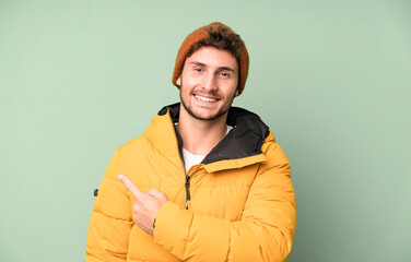 handsome teenager smiling cheerfully, feeling happy and pointing to the side. winter clothes and cold concept - obrazy, fototapety, plakaty