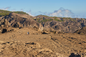 Pareja caminando en paisaje desértico con árboles de fondo, en Roque Nublo, Gran Canaria.