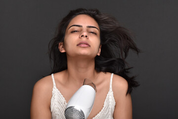 Happy young woman drying her hair using blower 