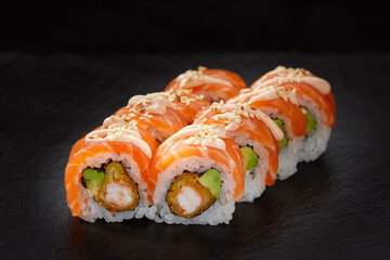 Vibrant sushi set, creative idea concept. Sushi California or Philadelphia rolls. Traditional Japanese cuisine concept. Sprinkled with sesame seeds. Over black background.
