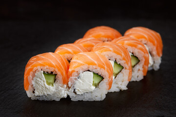 sushi roll with salmon, avocado and cream cheese on a black background.