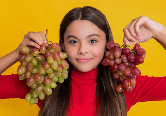 smiling teen girl hold bunch of grapes on yellow background