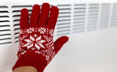 Woman warming her hand with a warm heater radiator in a cold winter day at home. Power saving, energy crisis background.