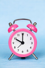 Pink alarm clock on a blue background. Save time, daylight savings.