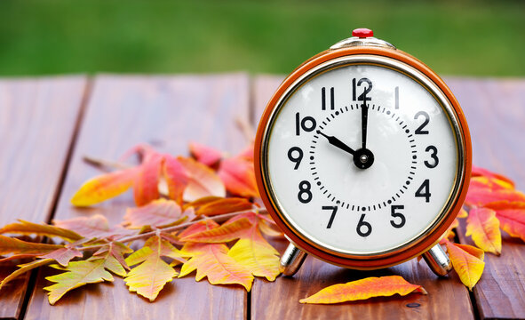 Retro alarm clock with orange autumn fall leaves, daylight savings time or halloween, thanksgiving background