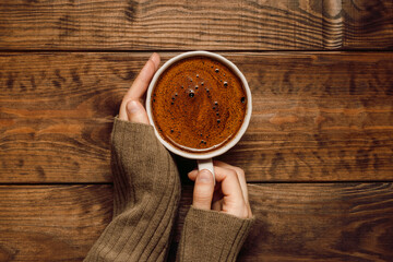 Hands hold cup of coffee close up on wooden dark background, top view, flat lay