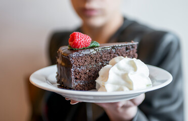 Woman showing chocolate cake with whipped cream, defocused backgroud