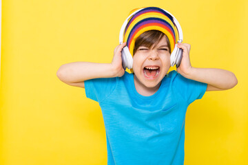 Handsome little boy in blue shirt and colorful hat with headphones, yellow background, banner