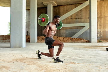 Athletic black young man lifting a heavy-weight barbell in outdoor gym under the bridge. Healthy lifestyle concept