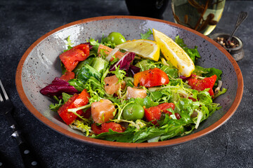 Fresh salad with salmon fish mixed with greens, tomato, olives, mustard and lemon juice