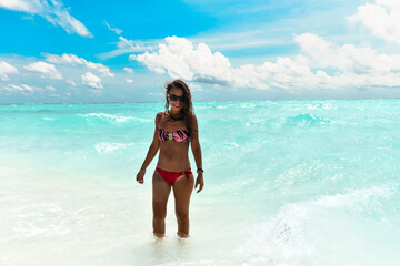 A joyful image of a young woman walking by the ocean, with waves touching her legs and feet, ideal for projects highlighting seaside relaxation, leisure, and the blissful connection to nature