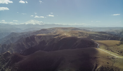 Naklejka premium Shooting from a quadrocopter with a view of the Caucasus mountains and the ridge, the white peak of Mount Elbrus stands out, in the foreground below is the road along the mountain ridge