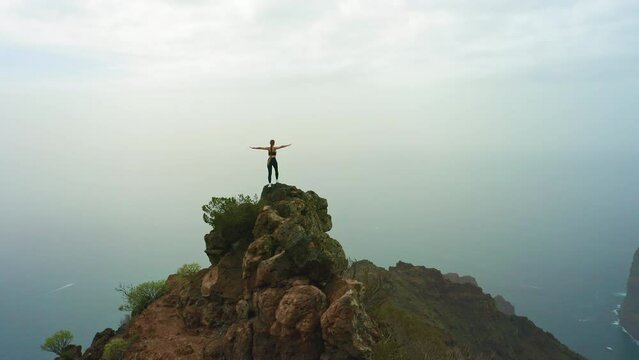 Cheering freedom woman hiker outstretching her arms at sunset mountain peak cliff edge