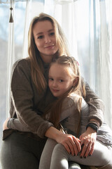 mom and little daughter are sitting at home against the background of the window