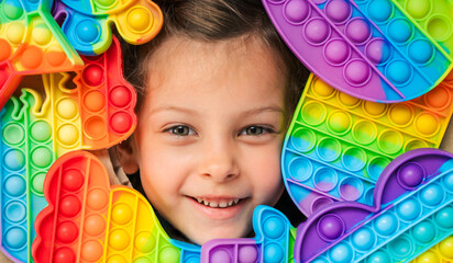 Little girl,kid,child head among many,lots of colorful pop it. Children play. Trendy silicone antistress colorful sensory push toy popit. Flapping fidget. Rainbow color.Cure of autism.Stress reliever