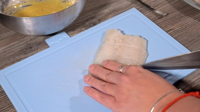 homemade fried fish in batter step by step. step 2 cutting white raw fish on the board with a large knife