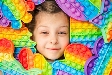 Little girl,kid,child head among many,lots of colorful pop it. Children play. Trendy silicone antistress colorful sensory push toy popit. Flapping fidget. Rainbow color.Cure of autism.Stress reliever