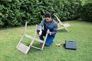 Handsome repairman fixing wooden furniture outside on the backyard	
