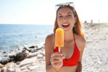 Attractive young woman offers a popsicle at the camera on summer. Focus on popsicle. - Powered by Adobe