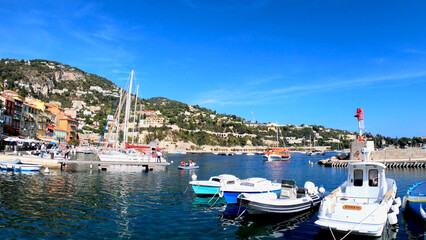 Fototapeta na wymiar Villefranche-sur-Mer, France, October 2, 2021: View of Port Villefranche-Santé with boats, catamarans, sails boats, speed boats, and yachts moored to the pier, during daytime with a clear blue sky.