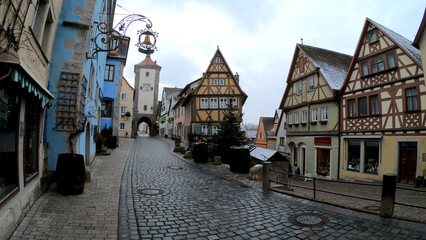 Fototapeta premium Rothenburg, Germany, December 9, 2021: The Plonlein. A yellow timber-frame house at the entrance of the Spital quarter and the two towers of the old city wall, Siebersturm and Kobolzeller Tor.