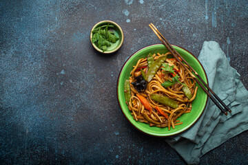 Asian dish stir fry udon noodles with chicken, vegetables and mushrooms in green ceramic bowl with...