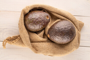 Two ripe avocados with jute bag on wooden table, macro, top view.