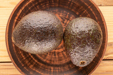Two ripe avocados with a clay plate on a wooden table, macro, top view.