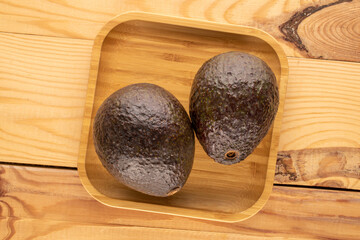 Two ripe avocados with bamboo plate on wooden table, macro, top view.