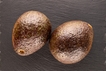 Two ripe avocados on slate stone, macro, top view.