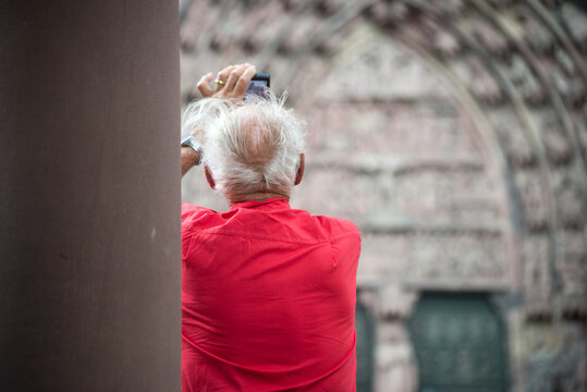 portrait on back view of old man taking a photo with his smartphone in the street