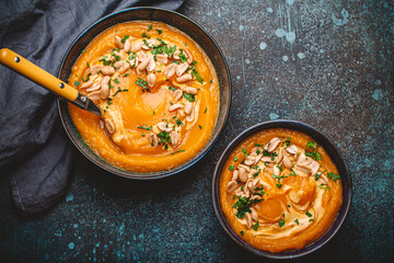 A ceramic bowl with pumpkin cream soup decorated with peanuts on dark stone background with spoon decorated, from above. Autumn cozy dinner concept 
