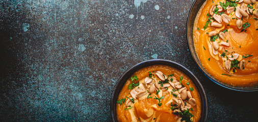 A ceramic bowl with pumpkin cream soup decorated with peanuts on dark stone background with spoon decorated, from above. Autumn cozy dinner concept 
