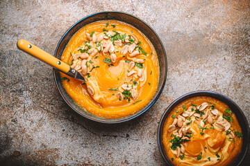 Ceramic bowl with pumpkin cream soup decorated with peanuts on rustic old metal oven tray...