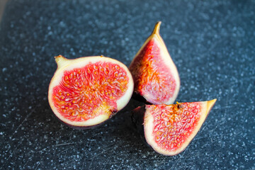 Close-up photo of a fig on a dark board. Ripe fruit whole and in pieces.