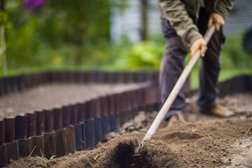 Farmer cultivating land in the garden with hand tools. Soil loosening. Gardening concept. Agricultural work on the plantation