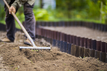 Farmer cultivating land in the garden with hand tools. Soil loosening. Gardening concept. Agricultural work on the plantation