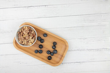 a bowl of granola and bilberry on wooden tray on wooden table flat lay