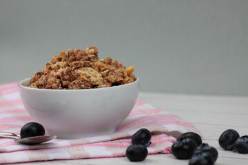 a bowl of granola, blueberry and spoon on a napkin on wooden background