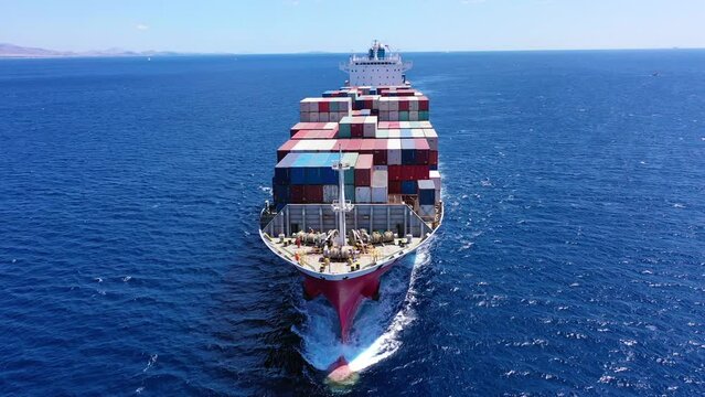 Aerial drone video of bow from container ship with colourful truck size containers cruising in open ocean Mediterranean Aegean sea, Greece