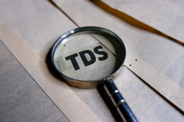 Concept of TDS or tax deduct at source with magnifying glass.