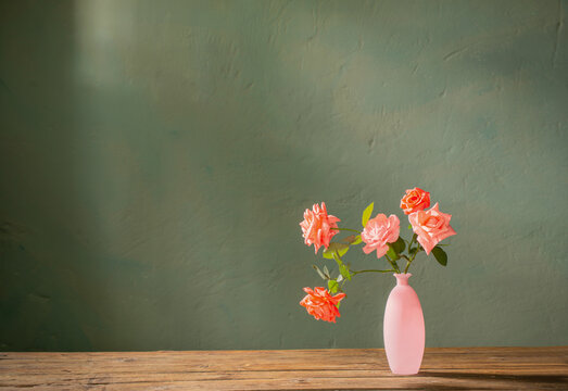 pink roses in glass pink vase on wooden table on background dark wall