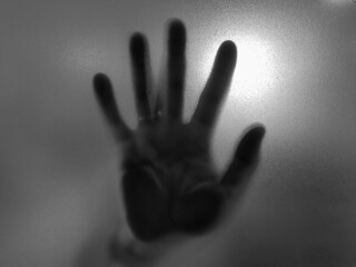 Black and white shadow image of hand behind the frosted glass sign of scary fear bad haunting...