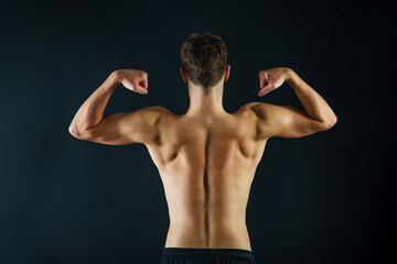 Fototapeta na wymiar A man making muscles with his arms from behind showing a muscular and fit back on a black background